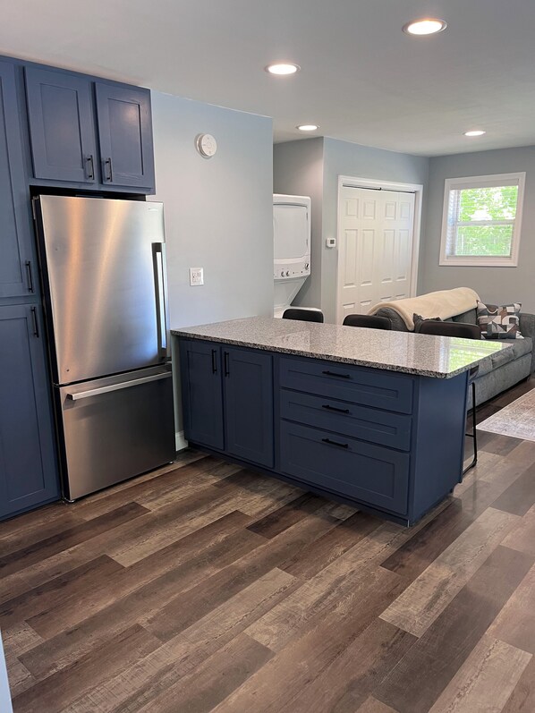 Una cocina moderna con un refrigerador de acero inoxidable, armarios azul oscuro y suelo de madera en patrón de espiga.