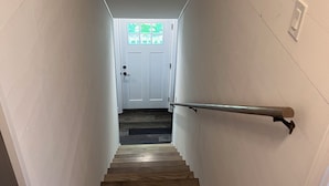 Una escalera de madera con barandilla, paredes blancas y una puerta al final.