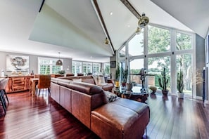 A spacious living room with a large leather sofa, a dining area, and a view of the outdoors through large windows.