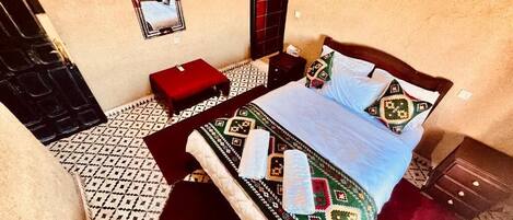 Un dormitorio con una cama, una mesita, un espejo y un suelo con estampado.