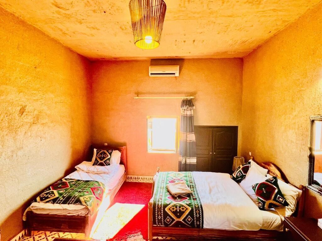 A room with two beds, a window with curtains, an air conditioning unit, and a hanging light fixture.