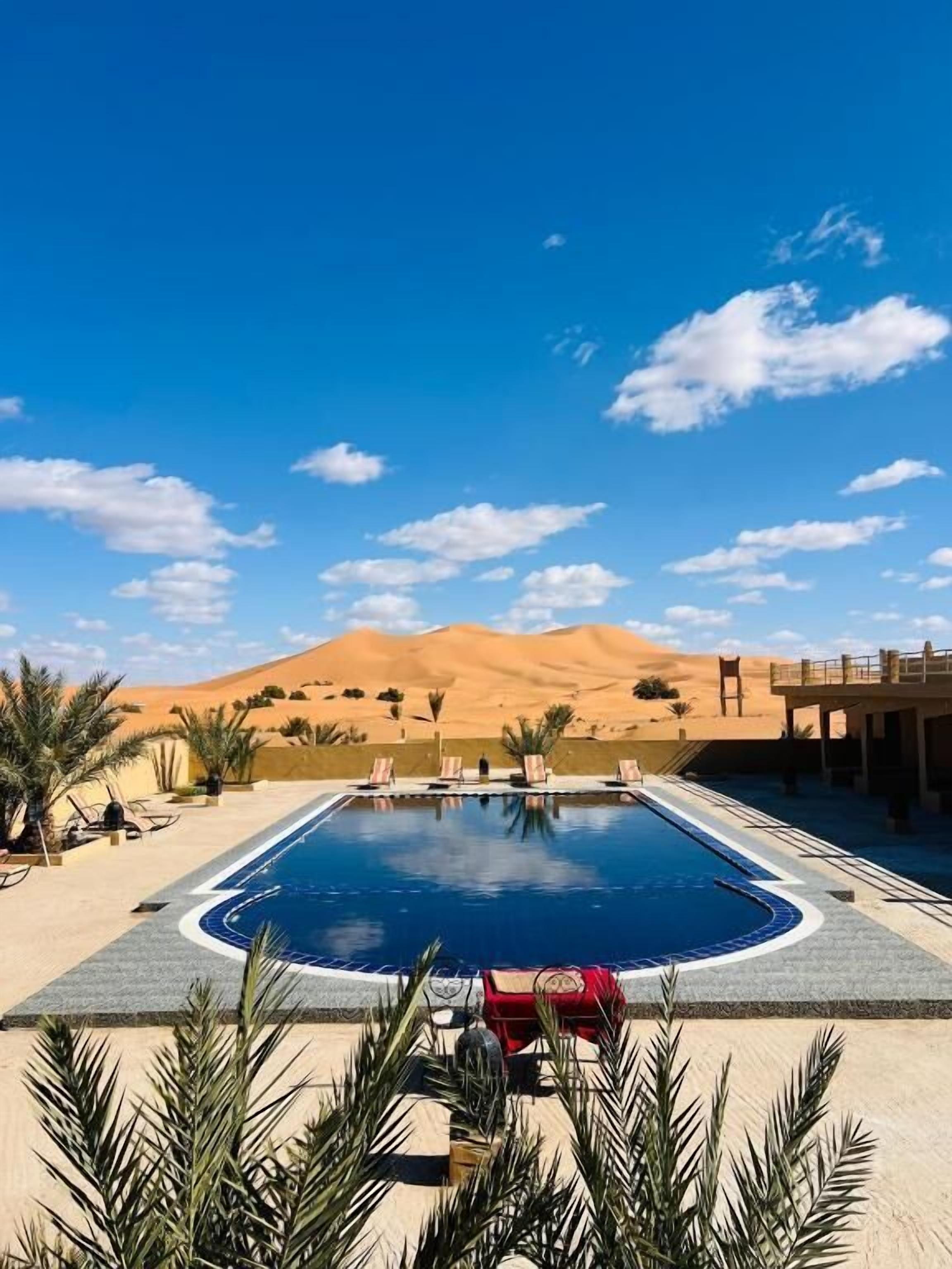 A swimming pool with lounge chairs, palm trees, and a desert landscape in the background.