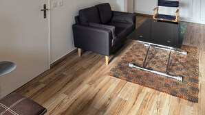 Una sala de estar moderna con un sofá, una mesa de centro de vidrio, piso de madera y una alfombra estampada.