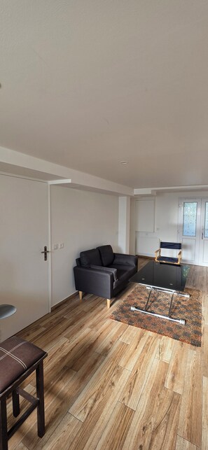 A modern living room with a sofa, a glass-top coffee table, a wooden floor, and a patterned rug. - Apartment with garden near Paris (Créteil)