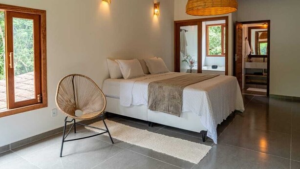 Un dormitorio con cama, dos luces empotradas, una silla de ratán, alfombra de cuero de vaca y techo de madera.