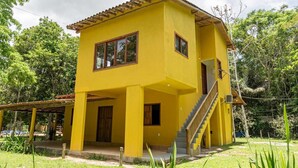 Un edificio amarillo de dos pisos con un porche cubierto, una escalera y una puerta.