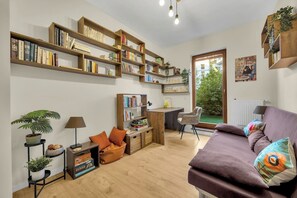Ein gemütliches Wohnzimmer mit einer Couch, einem Schreibtisch und einem Bücherregal voller Bücher.