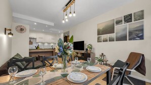 Un moderno comedor con una mesa de madera dispuesta para cuatro, un florero con flores y una cocina al fondo.