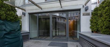 A modern building entrance with a glass door, a covered area with a green tarp, and a metal staircase.