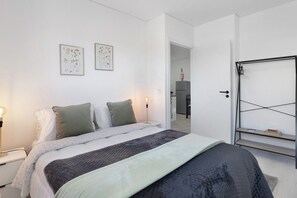 Une chambre à coucher comprenant un lit, des tables de chevet, une commode, une étagère fixée au mur et une porte donnant sur une autre pièce.