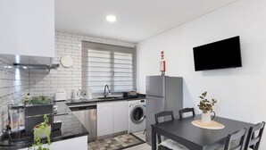 A modern kitchen with a built-in washing machine, a dining table with chairs, and a flat-screen TV mounted on the wall.