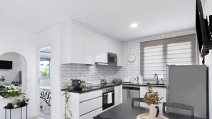 A modern kitchen with white cabinetry, a microwave, oven, and a dining area with a table and chairs.