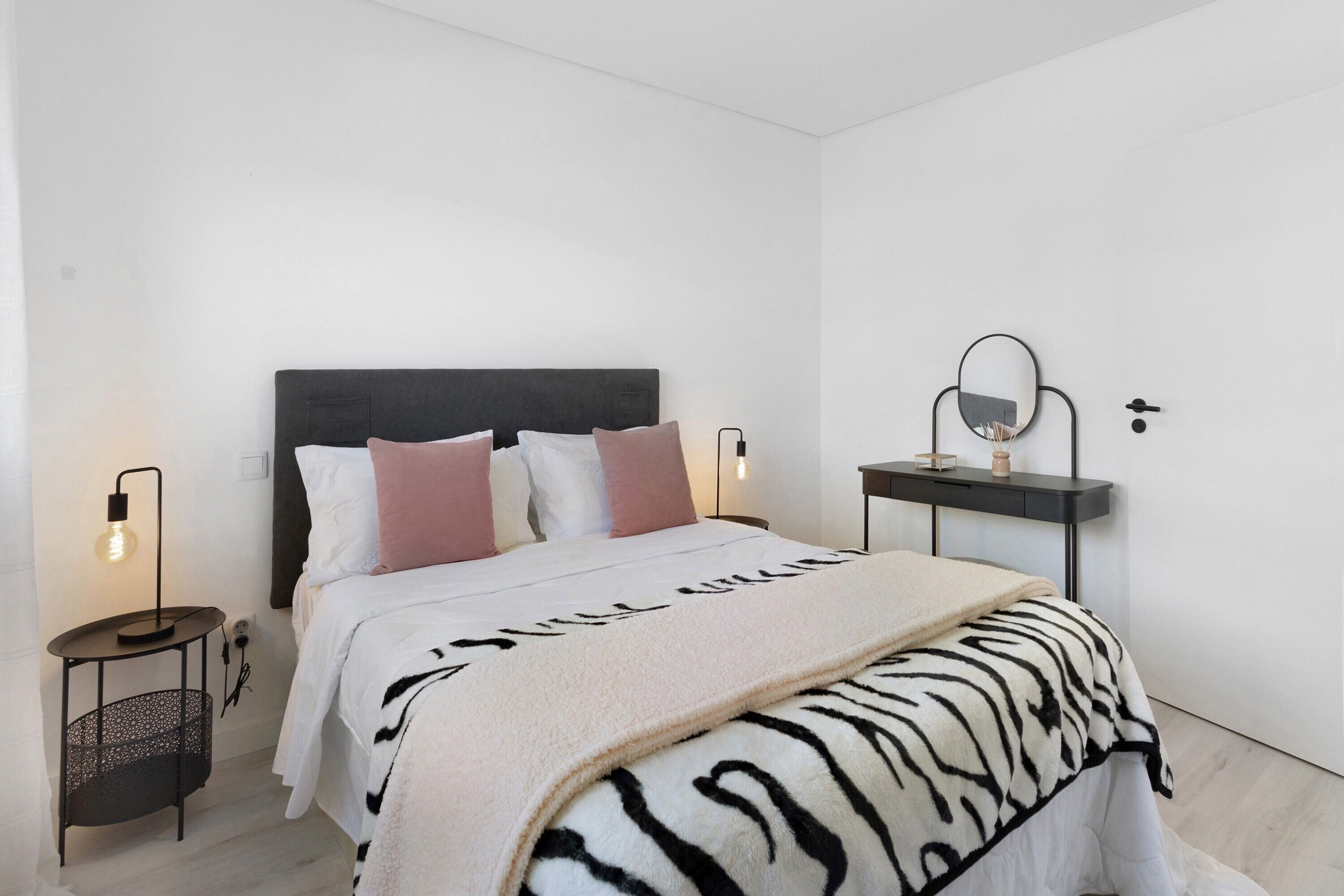 Een slaapkamer met een bed, nachtlampjes, een nachtkastje, een spiegel en een bijzettafeltje.