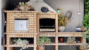 A brick-built outdoor oven with a small window, potted plants, and a metal grill pan on top.