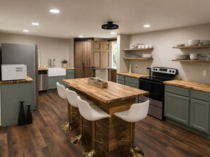 A modern kitchen with a central island, bar stools, a refrigerator, a stove, and wooden shelves.
