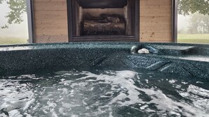 Una cabaña de madera con chimenea, un jacuzzi y vistas a los árboles.
