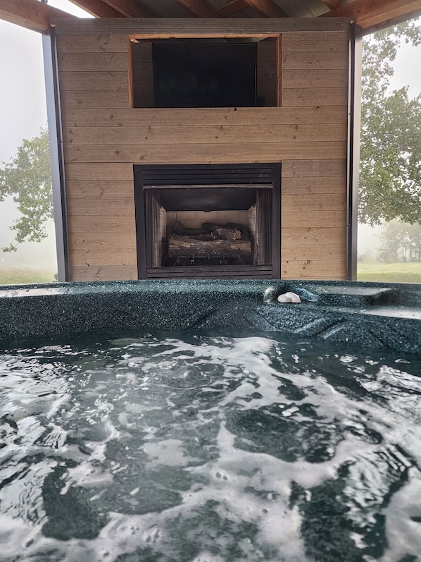 A wooden cabin with a fireplace, a hot tub, and a view of trees.