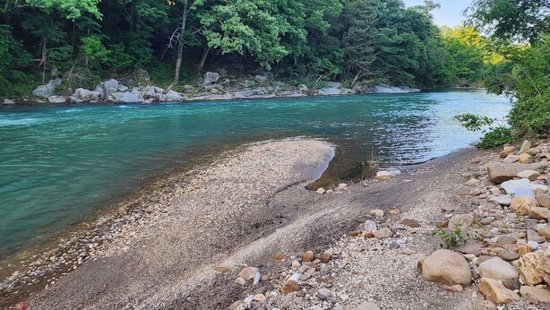 Un río de aguas claras, rodeado de rocas y árboles.