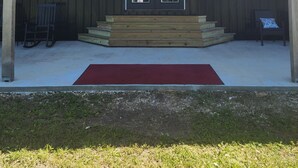 Un edificio de madera con un porche cubierto, una alfombra roja y dos sillas.