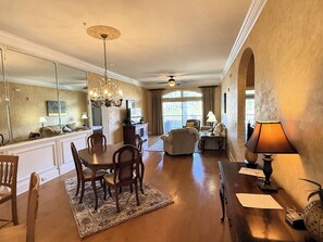 A spacious living room with a dining area, a chandelier, and a large mirror. - Gated Luxury Condo Overlooking The Intercoastal Waterway  & Centrally Located (Myrtle Beach)