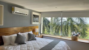 A neatly made bed with a headboard, a wall-mounted air conditioner, a framed picture, and a window with a view of palm trees. - Huatulco Loft 411 PG 5 minutes from El Arrocito Beach (El Arrocito, Huatulco)