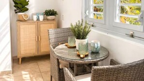 A sunlit room with a round glass table, wicker chairs, a cabinet with decorative items, and a window with a view of palm trees. - CasaMar Oceanfront House w/ Pool & Master Suite• Rincón (Aguada)
