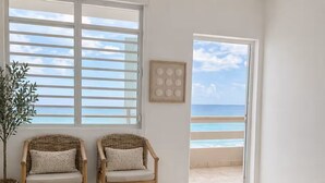 A bedroom with a bed, two wicker chairs, a potted plant, a rug, and a view of the ocean through a door. - CasaMar Oceanfront House w/ Pool & Master Suite• Rincón (Aguada)