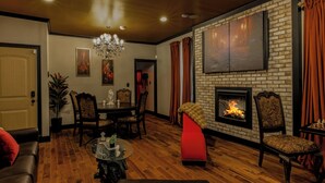 Un salon avec une cheminée, un plancher en bois, un lustre et un mur en briques.