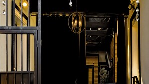 Un escalier menant à l’entrée d’un immeuble, avec une porte en métal, un luminaire suspendu et une rampe d’escalier.