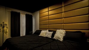 Une chambre à coucher avec un grand lit, une literie aux couleurs sombres, une tête de lit capitonnée et un lustre.
