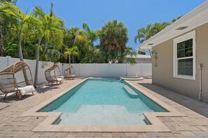 A rectangular swimming pool with a white deck, surrounded by a white fence, and equipped with wicker lounge chairs. - Sandcastle By The Sea (Holmes Beach)