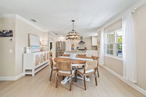 A modern kitchen with a central island, stainless steel appliances, and a dining area with a wooden table and chairs. - Sandcastle By The Sea (Holmes Beach)