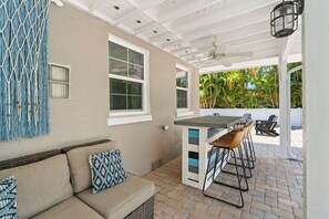 An outdoor patio area with a sofa, a table with chairs, and a view of palm trees. - Sandcastle By The Sea (Holmes Beach)
