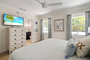A bedroom with a bed, a ceiling fan, a TV, a dresser, and a window with curtains. - Sandcastle By The Sea (Holmes Beach)
