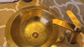 Un baño con un lavamanos dorado, un espejo y una toalla.