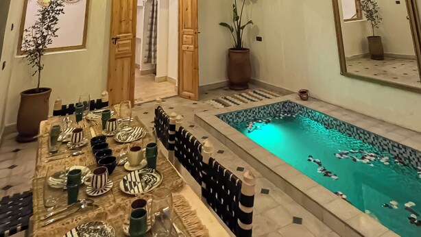 Un espacio interior amplio con piscina, zona de comedor y techo alto con iluminación decorativa.