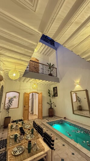 A spacious indoor area with a pool, a dining setup, and a high ceiling with decorative lighting. - Riad Nouha • Piscine privative • Toit-terrasse • Petit-déjeuner (Marrakech)
