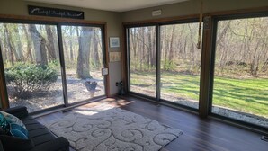 A room with large sliding glass doors, a dark-colored sofa, a patterned rug, and a small table with a decorative item. - Stunning 5-bedroom home on 18 acres with complete privacy, seclusion and nature (Burlington)