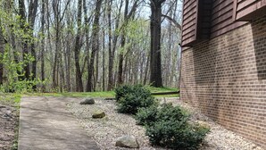 A concrete pathway leading to a brick building, surrounded by trees and small bushes. - Stunning 5-bedroom home on 18 acres with complete privacy, seclusion and nature (Burlington)