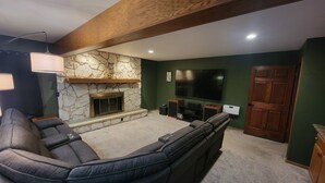 A living room with a stone fireplace, a large flat-screen TV, and a dark-colored sofa. - Stunning 5-bedroom home on 18 acres with complete privacy, seclusion and nature (Burlington)