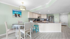 A modern kitchen with a central island, white cabinetry, and a dining area with a glass table and chairs. - Beautiful beach condo at Regatta Condominiums. 2 BR/2BA, Sleeps up to 6 adults. (Gulf Shores)