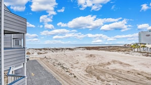 A beach view with a sandy path leading to the ocean, a wooden structure on the left, and a building with a sign on the right. - Beautiful beach condo at Regatta Condominiums. 2 BR/2BA, Sleeps up to 6 adults. (Gulf Shores)