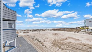 A beach view with a sandy path leading to the ocean, a wooden structure on the left, and a building with a sign on the right. - Beautiful beach condo at Regatta Condominiums. 2 BR/2BA, Sleeps up to 6 adults. (Gulf Shores)