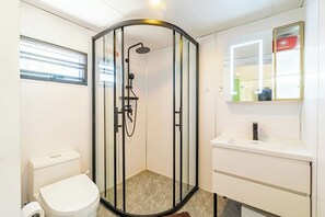 Kylpyhuoneessa on lasiseinällä varustettu suihku, wc ja pesuallas, jonka yläpuolella on peili.