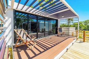 Una terraza moderna al aire libre con cerramiento de vidrio, piso de madera y dos sillones de lounge.