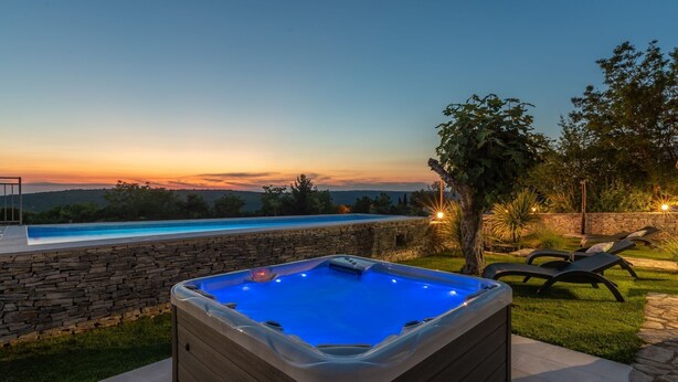 Ein Whirlpool mit Steinwand und Pool, umgeben von einer Rasenfläche und Bäumen.