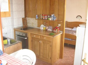 A compact kitchen with wooden cabinets, a sink, a stove, and a small dining area with a table and chair. - Apartment Riva - Two Bedroom Apartment with Sea View (1) (Lastovo)