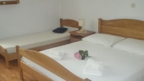 Een kamer met twee houten bedden, één groter en één kleiner, elk met witte lakens en kussens. Er staat een nachtkastje met een lamp en een kleine plant bij het grotere bed.