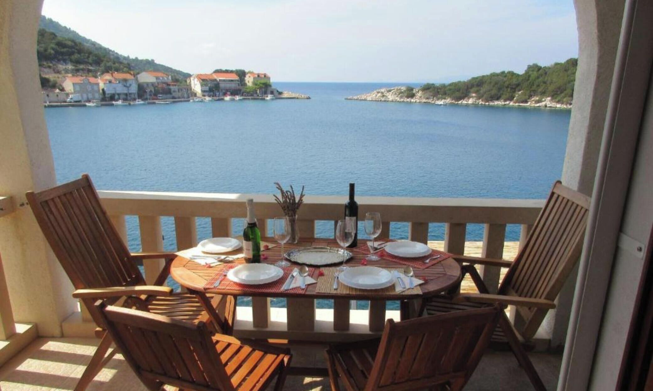 Une table dressée pour deux personnes, avec vue sur une mer calme et des bâtiments éloignés.