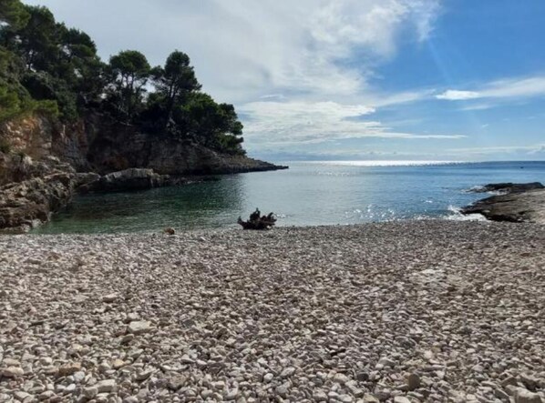 Ein Kiesstrand mit felsigen Klippen und Bäumen im Hintergrund.